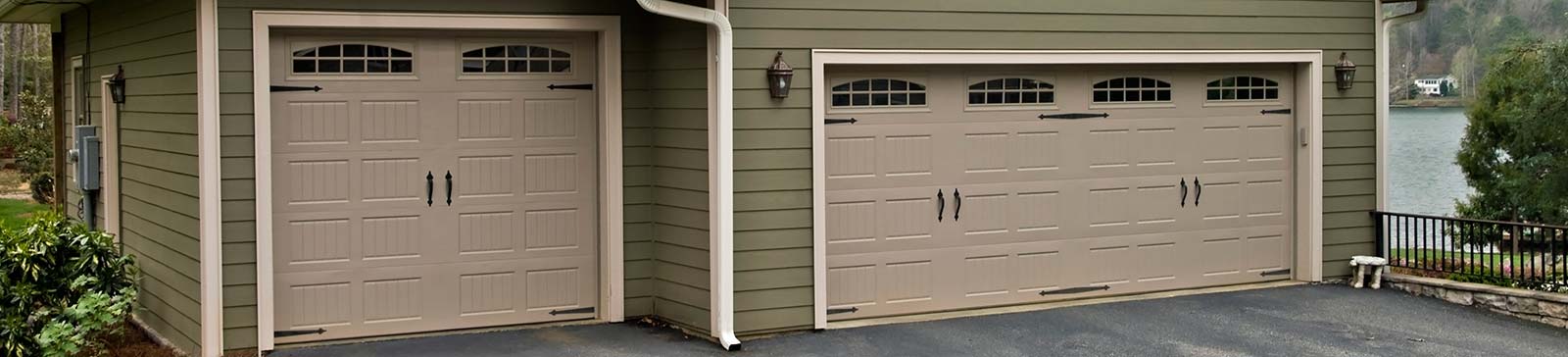 Beige traditional carriage-style garage doors with windows and black hardware on green house