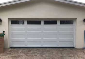 Modern white sectional garage door installed in Flushing NY home with three glass windows on top panel