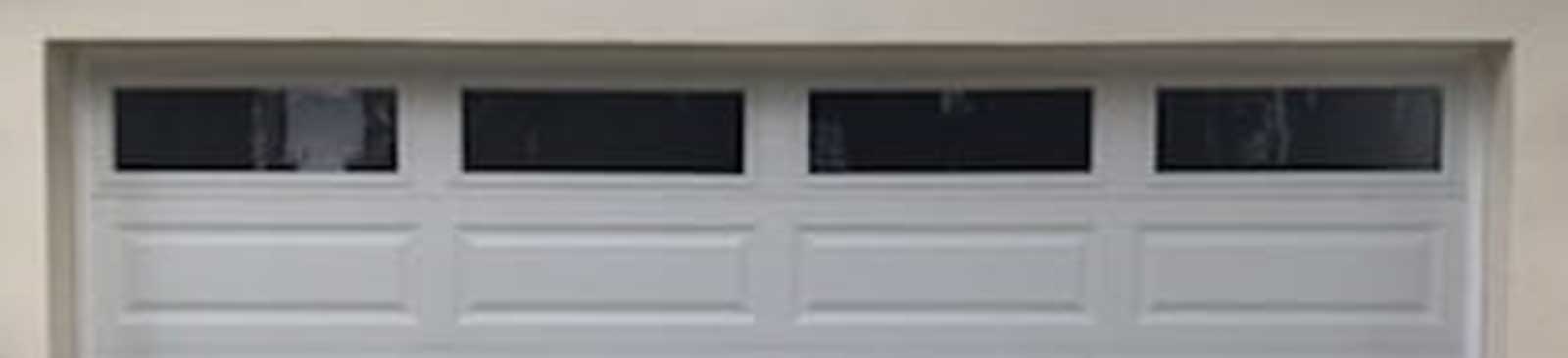 Modern white sectional garage door installed in Flushing NY home with three glass windows on top panel